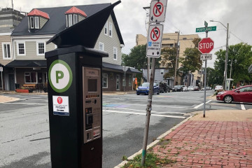 A parking meter is seen on a brick sidewalk alongside a road with a stop sign in the distance. 