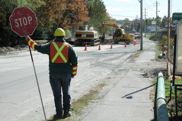 A worker wearing a high-vis vest and hard hat directs traffic and holds up a stop sign.