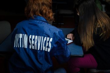 Photo taken from behind of Victim Services volunteer wearing a navy blue jacket with Victim Service in white lettering on the back.