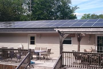 Multiple solar panels on a house roof house has large deck with lots of deck furniture