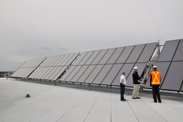 three employees stand next to very large solar panels on the top of a building