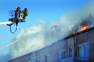 Two firefighters spray a structure fire from the bucket of a fire truck