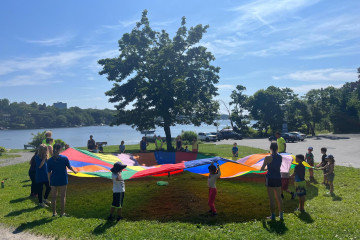 Grooup of children playing outdoors by the Northwest Arm with a parachute. 