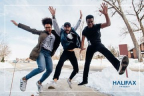 Three teenagers smiling and jumping into the air with their hands up. They are outdoors and snow is on the ground. 