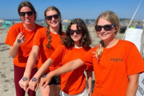 Four recreation staff wearing orange t-shirts standing on a beach showing off temporary tattoos on their hands