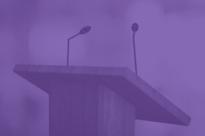 A purple image with a microphone at a podium. 