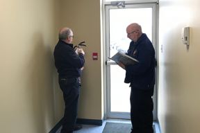 Image of two Halifax Regional Fire & Emergency Fire Prevention Officers conducting an inspection of a building. One is looking closely at a portable fire extinguisher while the other makes notes.