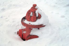 Close up image of a red fire hydrant buried in snow about half of the way up.