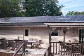 Multiple solar panels on a house roof house has large deck with lots of deck furniture
