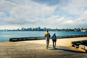 Man and woman walking on the Dartmouth boardwalk with Halifax skyline in view