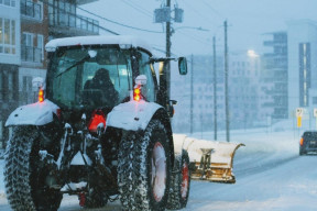 A tractor travels away from the camera on a wintery evening.