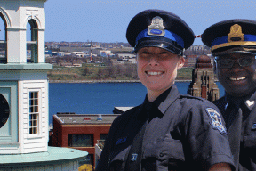 Photo of a male and female officer in front of the Town Clock on Citadel Hill with the Halifax skyline in the background