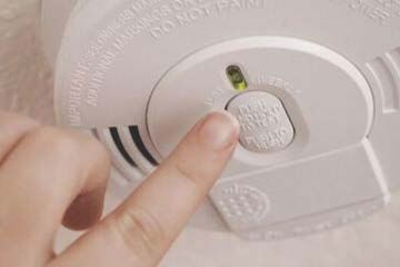 Photo of a finger pointing to a smoke alarm button to indicate make sure your smoke alarms work. 