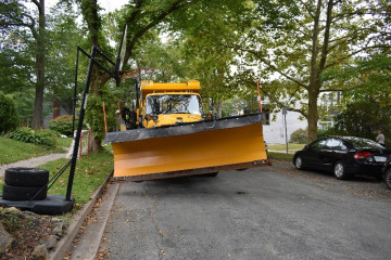Truck with snowplow attached, driving on residential road with a basketball net on the curb.